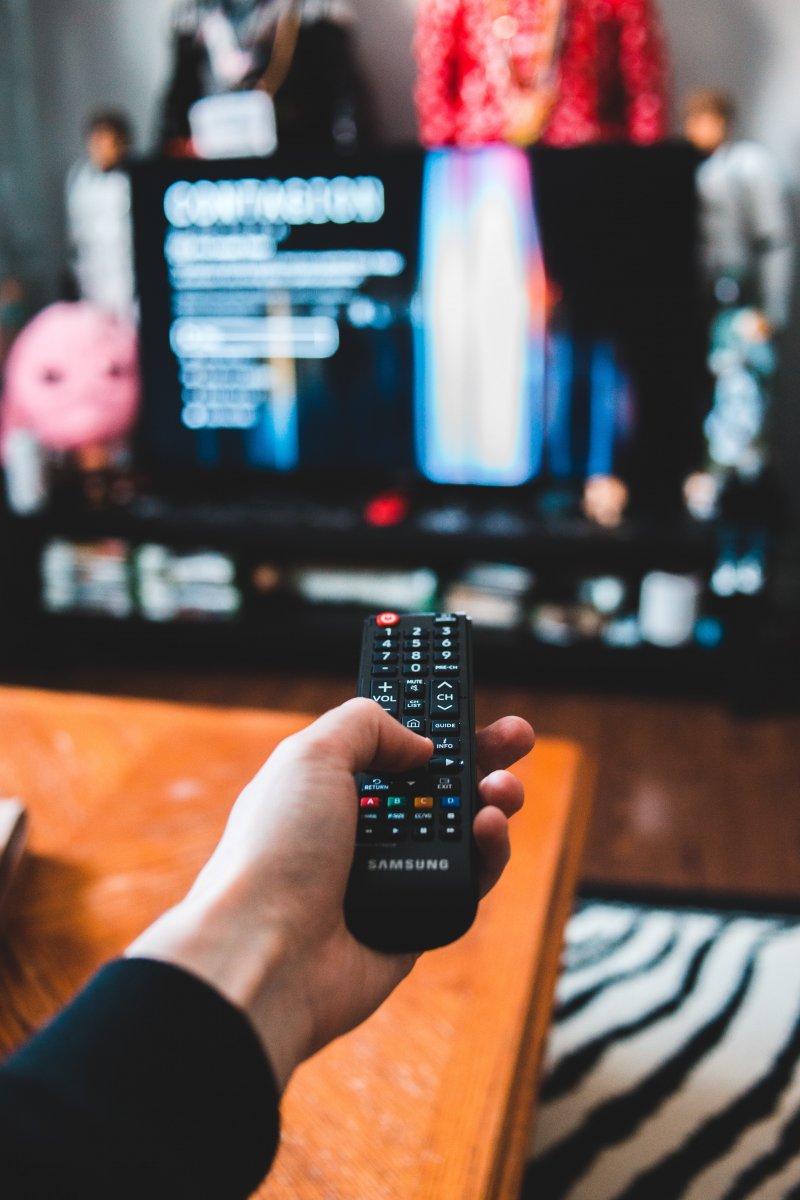 Image of person holding a remote watching TV by Erik Mclean on Unsplash