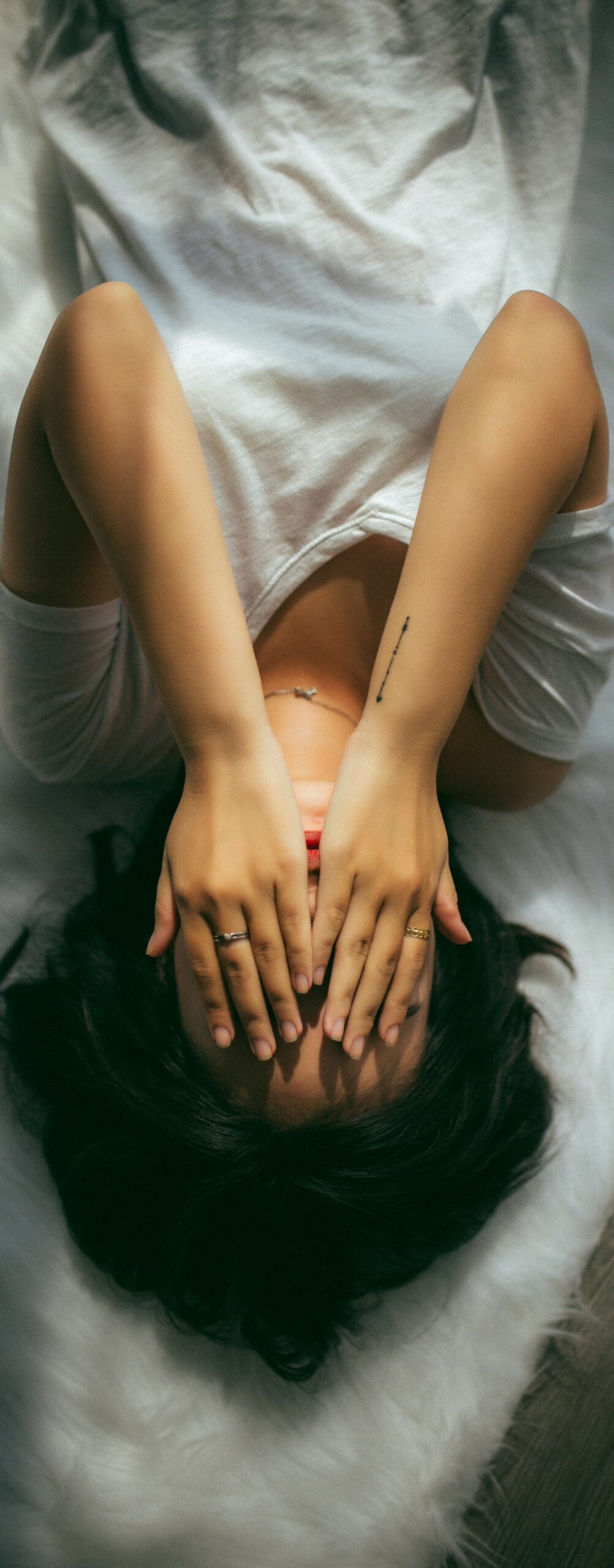 Image of woman covering her face in stress while laying in bed