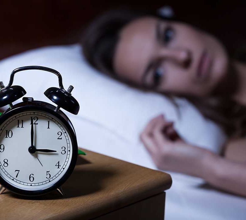 Image of sleep-deprived woman laying in bed staring at a clock