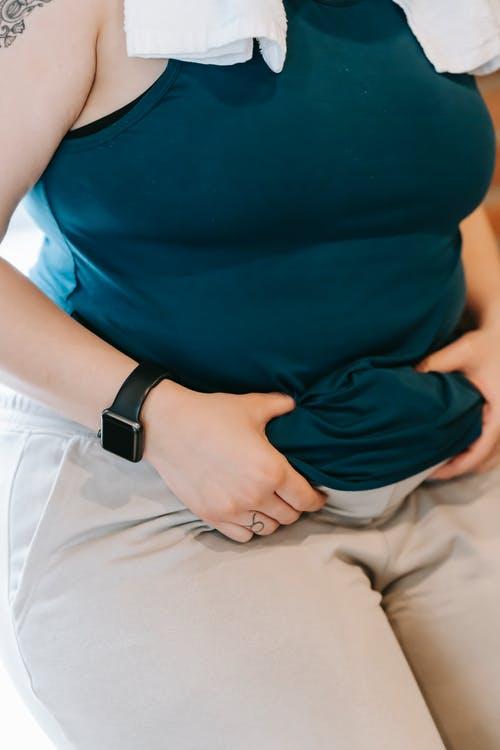 A woman holds her tummy rolls, showing belly fat and concerns.