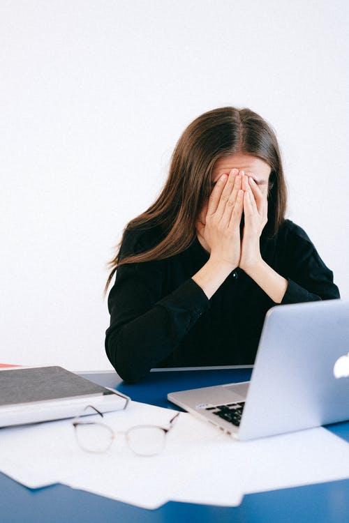 A woman is sitting at her desk during work while covering her face.